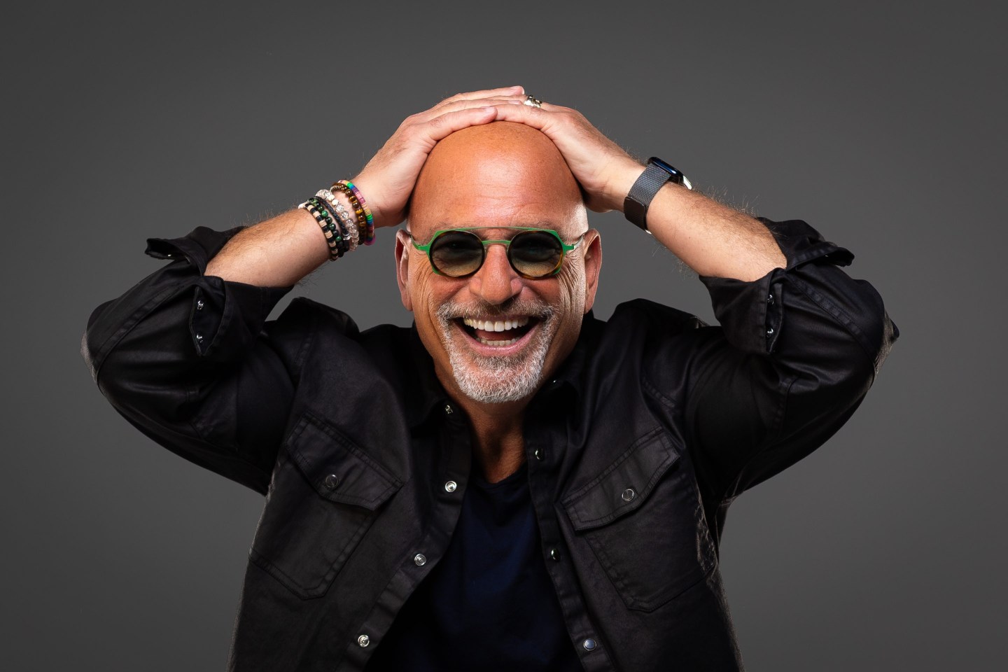 Howie Mandel smiling with his hands resting on his head
